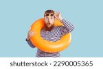 Small photo of Astonished funky crazy man with inflatable swimming circle isolated on pastel turquoise background. Chubby red-bearded man in striped sailor clothes looks at camera in shock, raising his sunglasses.