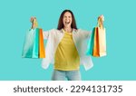 Small photo of Joyful woman with colorful packets shouts excited from her shopping at seasonal sales. Casual woman with closed eyes squeaking loudly while holding shopping bags on light blue background. Banner