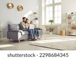 Small photo of Happy family spend time in spacious room at home. Couple with child watch online movie on laptop sitting on sofa in cozy light living place space with white grey walls, shelves, house plants and wifi