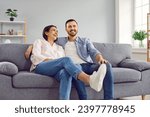 Small photo of Young family couple having fun at home. Happy husband and wife sitting on a comfortable grey couch and laughing. Cheerful husband and wife sitting on the sofa and laughing at a funny joke