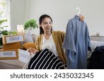 Small photo of Young Asian women sit in living room sorting clothes for donation in a donation box second hand clothes. Donate concept