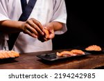 Small photo of Chef's hand holding fresh piece of salmon.Closeup of chef hands preparing japanese food. Japanese chef making sushi at restaurant.Chef making traditional japanese sushi on wood board.
