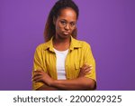 Small photo of Young offended ethnic African American woman pouting and crossing arms in front of chest looking at camera after bullying or insult or intolerance stands in studio with purple background