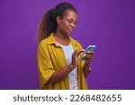 Small photo of Young attractive African American woman millennial with phone in hands spends all free time on smartphone suffering from gadget addiction and in need of psychological help stands on lilac background