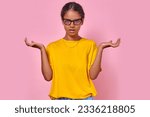 Small photo of Young finicky Indian woman of school age spreads arms to sides and looks at camera with displeased emotions demonstrating problems of adolescence and teenage selfishness stands in pink studio.