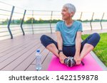Relaxed athletic mature woman sitting on fitness mat outdoors. Senior Woman Resting After Exercises. Woman on a yoga mat to relax outdoor. Senior lady prefers healthy lifestyle