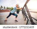 Small photo of Smiling retired woman stretching legs outdoors. Senior woman enjoying daily routine warming up before running at morning. Sporty lady doing leg stretches before workout