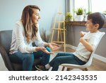 Small photo of Cheerful young kid talking with helpful child counselor during psychotherapy session in children mental health center. Child counselor during psychotherapy session