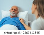 Small photo of Sick man looking at upset daughter while lying on bed in hospital. Daughter holding hand of father lying on bed in hospital. Displeased elderly man holding hand of blurred daughter while lying