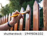 Small photo of Man painting wood stain at timber plank in garden. Paint protective varnish on wooden picket fence at backyard