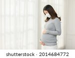 Happy Pregnant Woman turtleneck sweatshirt wear medical face mask protect virus standing in front of windows stroking big belly with love at cozy home,Pregnancy of young woman enjoy with future life