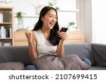 Small photo of Millennial asian young woman looking mobile phone laughing with good news or discount voucher for shopping online at home.Happy and cheerful woman looking on cellphone app read message feel excited