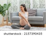 Happy Calm Pregnant Woman sit on yoga mat and stretching warm up for yoga practice,Pregnancy of young woman enjoy with yoga to breathing and meditation at home,Motherhood and Wellness Pregnant Concept