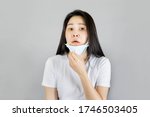 Small photo of Young Asian woman wearing medical face mask and white t shirt her hands pull the mask down Inconvenient breathing, feeling uncomfortable isolated on gray background,health care concept