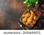 Fried crispy chicken legs in breadcrumbs on a wooden serving board on a dark background. Fast food from the drumstick top view	