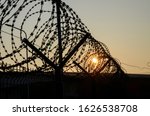 Close-up of sharp razor wire fence at sunset. Barbed tape. Rusty metal barbered wire on jail. Concept of prison, immigration, detention, boundary or war. Prison barber wire near jail or camp.