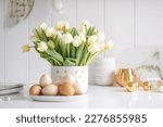 Small photo of Easter table setting with tulips, Easter bunnies, and eggs with golden patterns in the white Scandinavian-style kitchen background. Beautiful minimalist design for greeting card.