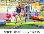 Boy in protective gear holding safety rope and passing obstacle course in indoor adventure park