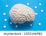 Small photo of 3D anatomical model of brain is on blue background surrounded by white pills as ornament polka dots. Medical concept by pharmacological tablet treating brain diseases, pharmacotherapy, chemotherapy