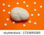 Small photo of 3D anatomical model of brain is on orange background surrounded by white pills as ornament polka dots. Medical concept by pharmacological tableted treat of brain and neurology disease pharmacotherapy