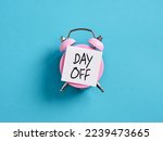 Business Day Off Annual Leave, Relaxation, Holiday or Vacation Concept. Pink alarm clock with a note paper on blue background with the message day off.