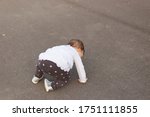Small photo of One year old baby girl falling on asphalt and trying to get up. Toddler tumbled down on her knees and hands. Learning to walk. Back view.