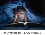 Small photo of happy boy is lying under blanket and reading book in dark with flashlight, instead of sleeping, at time when everyone is asleep, night. kid hid from everyone. Thirst for knowledge.