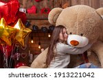 attractive young woman in a beautiful background for a photo shoot on Valentine's Day, cuddling with huge teddy bear, a wooden fireplace with candles and flowers, and a tree with red and pink hearts.