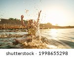happy little girl splashes in water near shore. Summer children's vacation on shore lake or river. child jumps into water, swims, splashes at sunset. Active recreation. Dynamic image. Selective focus