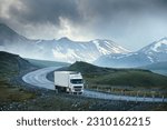 Small photo of Large white transport truck transporting commercial cargo in semi trailer running on turning way highway road with scenic mountains mountaineous scenery in background.