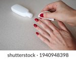 Small photo of girl removes red nail polish on a light background with a bottle of nail polish remover