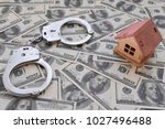 Small photo of iron handcuffs, a house made of wood on a background of American dollar bills. illegal sale of property. swindle. economic crimes.