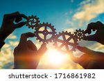 Small photo of Four hands of businessmen connect gears to a puzzle on a background of sunset. Business concept idea, partnership, cooperation, teamwork, community, creative