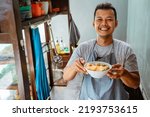 Small photo of man seller smiling while bringing a bowl of chicken noodles for customers in a stall cart