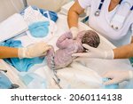 Small photo of Baby being born via Caesarean Section coming out or baby minutes after the birth. Unrecognizable doctors examines a newborn baby boy in the first few minutes of life at hospital.