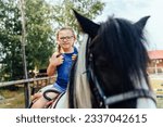 Small photo of Portrait of little cute girl with two braids walking with a pony in manege at open air outdoor. Human and horse friendship, hippotherapy and recreation concept.