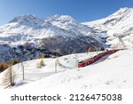 Small photo of Alp Grum, Switzerland - November 05. 2021 : Red train from Rhaetian Railway is passing the train tracks with tight 180° curve at high Alp Grum. The Piz Palu peak is at the background.