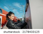 Happy brunette girl putting coin into ticket machine at railway station.