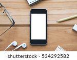 Mockup image of spectacles notebook pencil rubber earphones ruler with black mobile phone and blank white screen on wooden table background