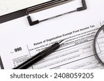 Small photo of Form 990 Return of organization exempt from income tax on A4 tablet lies on office table with pen and magnifying glass close up