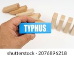 Small photo of Medicine and health concept. In the background there are wooden planks - half are standing, half are lying. In the hands of a blue plaque with the inscription - TYPHUS