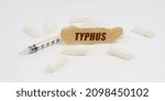 Small photo of Medicine and health concept. On a white table are pills, a syringe and a piece of paper with the inscription - TYPHUS