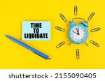 Small photo of Business concept. On the yellow surface there is an alarm clock, a pen and stickers with the inscription - Time to Liquidate