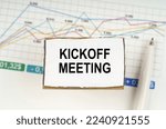 Small photo of Business concept. Against the background of business graphics and pens, a sign with the inscription - Kickoff Meeting
