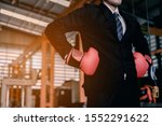 Small photo of A young business man in a suit, shirt and tie at an industrial factory He wears boxing gloves, demonstrating unceasing preparation for the fight for business progress.