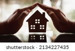 Small photo of Hands of a young woman surround a wood house model. Real estate agent offer house, property insurance and security, affordable housing concepts