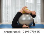 Asian young woman in sportswear doing abs exercises on a fitness ball for healthcare slim fit and body weight control at home. Female athletic practice yoga workout training by lotus position on ball.