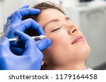 Attractive young woman is getting a rejuvenating facial injections. She is sitting calmly at clinic. The expert beautician is filling female wrinkles by hyaluronic acid.