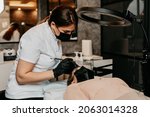 Small photo of Cosmetologist measures the proportions of the eyebrows with the ruler. Micropigmentation work flow in a beauty salon. Beautician and client are wearing face protective masks due to Covid-19 pandemic.