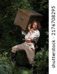 Small photo of Sea robber ship captain armed pirate goes through jungle with chest of treasures. Concept historical halloween. Filibuster cosplay.